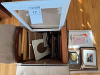 open box of assorted frames, white large frame, stack of framed prints