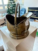 Angled view of hammered brass coal scuttle showing handle, pouring lip and base