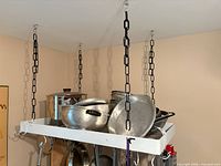 Full view of ceiling-mounted pot rack with chains and cookware on top