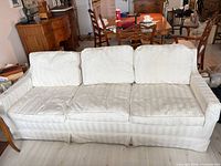 Full frontal view of ivory three-seat sofa with skirted base and rolled arms