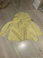 Yellow knit hooded newborn sweater laid flat