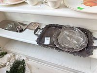 Shelf view showing stainless butter dish, ceramic dish, stacked silver-plated trays and glass relish dish