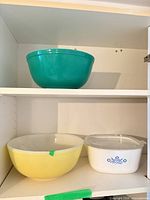 Green bowl, yellow bowl, white cornflower casserole with lid on shelves