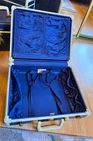 Suitcase open showing blue satin interior with tie-down straps and pockets