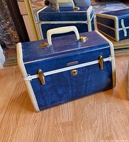 Front view of closed blue Samsonite train case showing handle, cream trim and brass lock