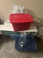 Overall lot showing plastic totes, boxed 4.5-ft tree, white tree branches, glass beverage dispenser
