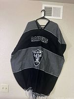 Full view of black/gray Raiders poncho on hanger showing fringe and overall design