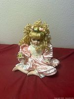 Full view of seated porcelain doll on red surface