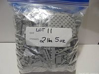 Front view of sealed bag showing assorted light bluish grey LEGO pieces and handwritten weight label