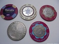 Five gaming pieces laid out showing fronts: four chips and one metal token