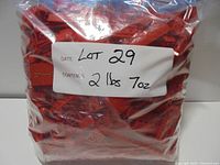 Sealed clear bag filled with red LEGO pieces, label shows lot number and weight 2 lbs 7 oz