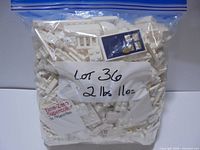Front view of sealed zipper bag filled with white LEGO pieces, label shows lot number and weight