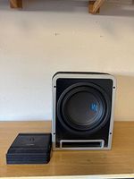 Front view of Alpine subwoofer in enclosure beside amplifier