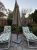 Full view of umbrella with base between two lounge chairs