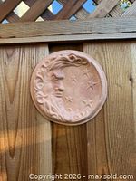 Full view of round terracotta moon and stars plaque on wood fence