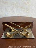 Front view showing crossed gold-tone golf clubs and mirrored plate