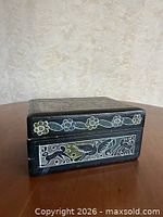 Front-side view of black rectangular box showing floral border and animal panel