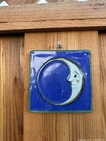 Front view of square ceramic tile showing crescent moon face motif on blue background