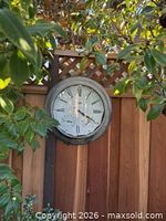 Clock mounted on wooden fence surrounded by foliage