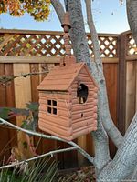Front view of terracotta log-cabin birdhouse hanging from tree