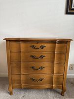 Front view showing four drawers, brass-tone handles, serpentine shape, cabriole legs