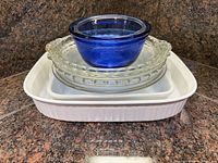 Stacked view of blue glass bowl, two clear glass pie plates, medium and large white ceramic bakers