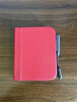 Closed red folio cover with Barnes & Noble Nook eReader and attached charging cable on wooden surface