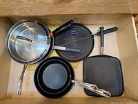 Drawer view showing stainless saucepan with lid, grill pan, small saucepan, square griddle, pot holder
