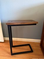 Full view of C-shaped black metal side table with brown wood top