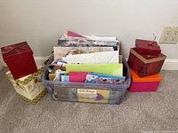 Plastic tote filled with gift bags, tissue paper and ribbon, flanked by decorative gift boxes