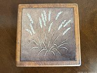 Top view of square wood-framed ceramic trivet showing wheat design