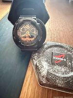 Watch seated in foam with open metal tin lid showing G-Shock logo