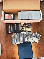 Open cardboard storage box with large stack of loose Magic cards and several cards spread out