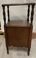 Front view of wooden side table showing upper shelf, cabinet door, turned legs