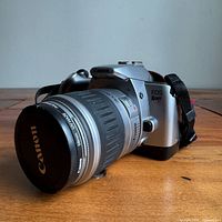 Camera front left view showing body, lens, cap, strap