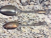 Top and bottom view of both ornate silver plated spoons on countertop