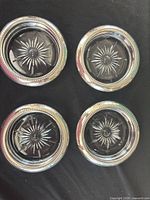 Top view of all four silver-plated glass coasters showing starburst centers and beaded rims