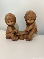 Front view of resin figurine showing boy and girl on seesaw