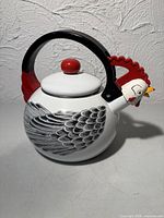 Front view showing rooster face spout, wing design, lid and handle
