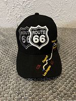Front view of black Route 66 embroidered baseball cap showing shield logos and route map on brim