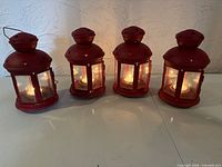 Four red metal and glass lanterns lit with tealights