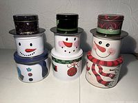 Nine tins stacked in three snowman sets showing full designs