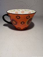 Mug left side view showing orange exterior floral design and black handle