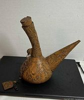Side view of tooled leather ewer showing spout, neck and embossed design