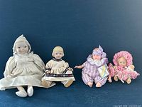 Front view of all four dolls seated side by side showing sizes, outfits and overall condition