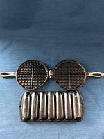 Open waffle iron showing grid plates and cornstick pan front