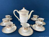 Full set arranged: coffee pot centered, seven cup-and-saucer pairs around
