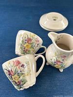 Two teacups and footed creamer showing floral pattern and shape