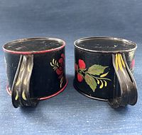 Two black tin cups side by side showing painted handles and bases