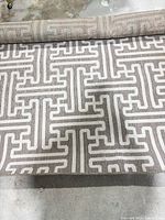 Rolled polypropylene rug showing beige/taupe geometric pattern and edge detail